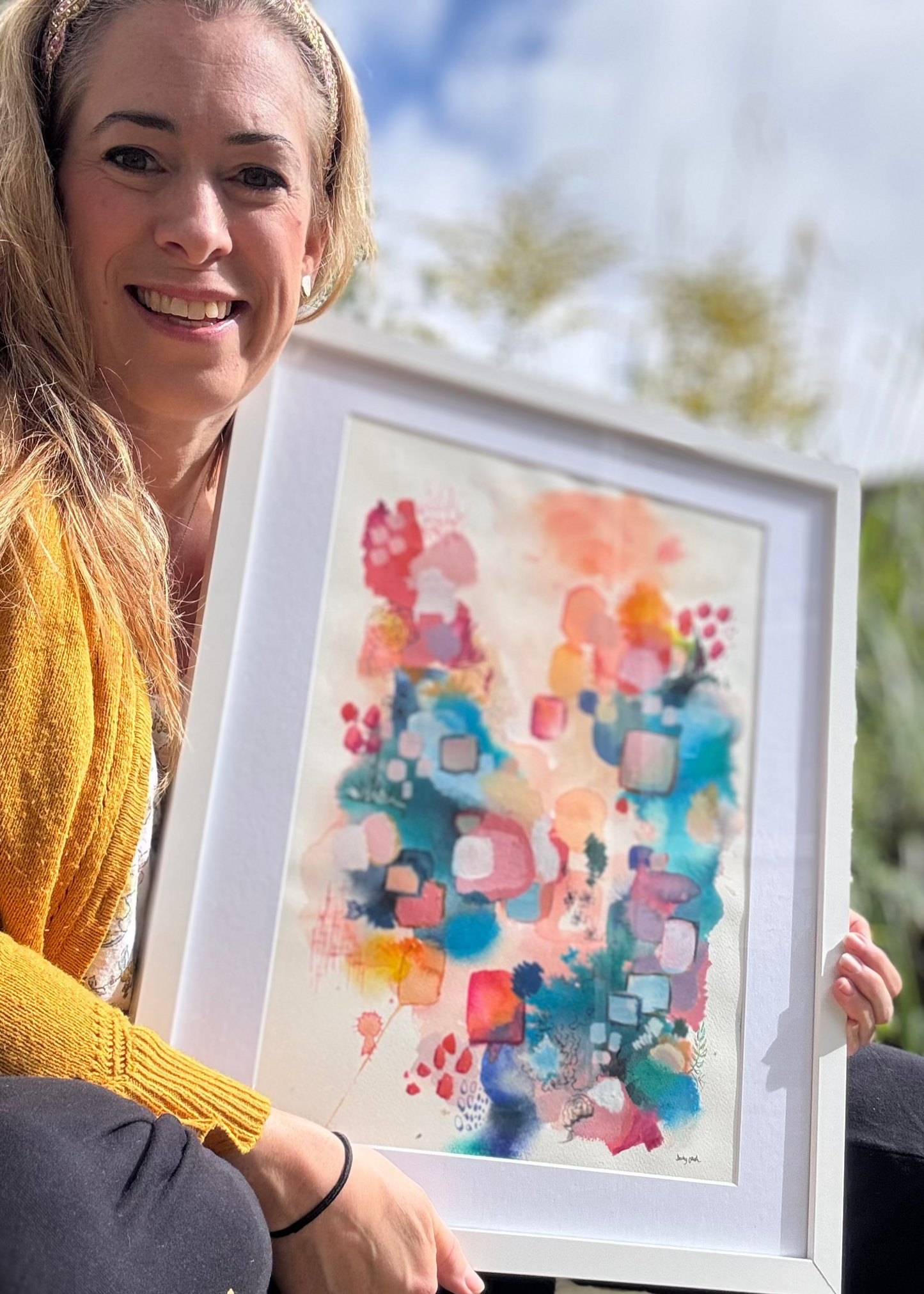 Woman holding a framed colorful abstract painting outdoors