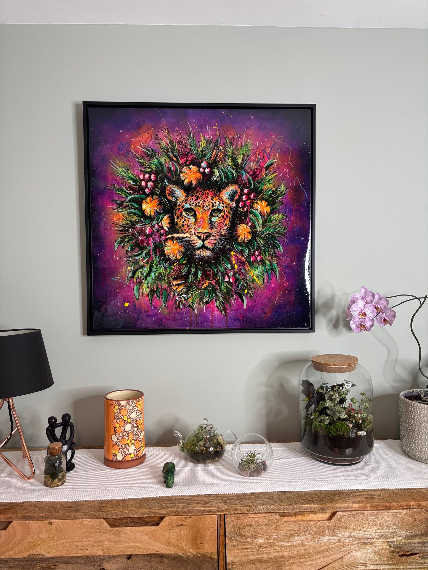 Framed artwork with vibrant wreath and leopards head in centre