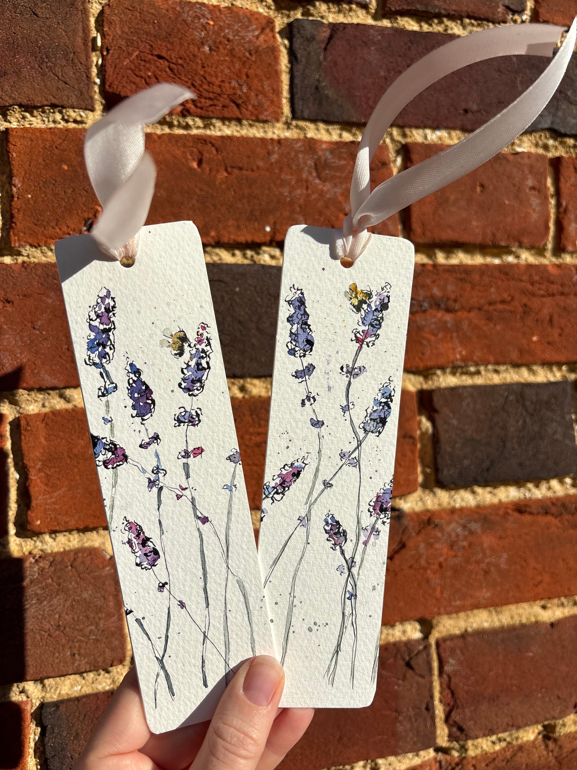 Two white tags with lavender  and bee designs held against a brick background