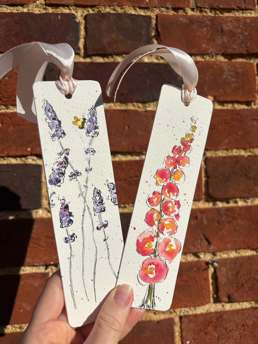 Two floral bookmarks with ribbons against a brick wall background