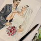 A custom watercolor wedding portrait of a bride and groom on textured paper, with a paintbrush resting on the bottom right corner.