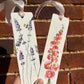 Two floral bookmarks with ribbons against a brick wall background