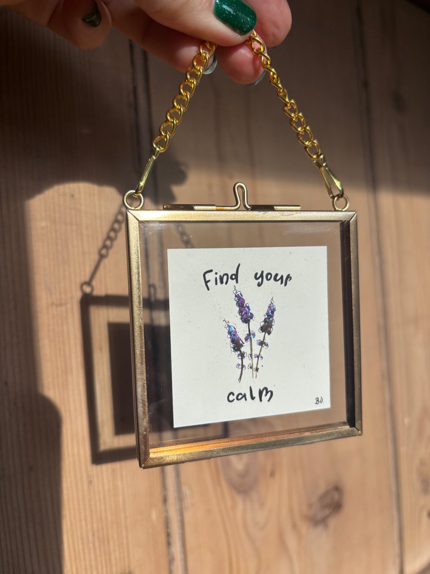 Tiny gold frame with small painting of some lavender with writing saying "Find your Calm"