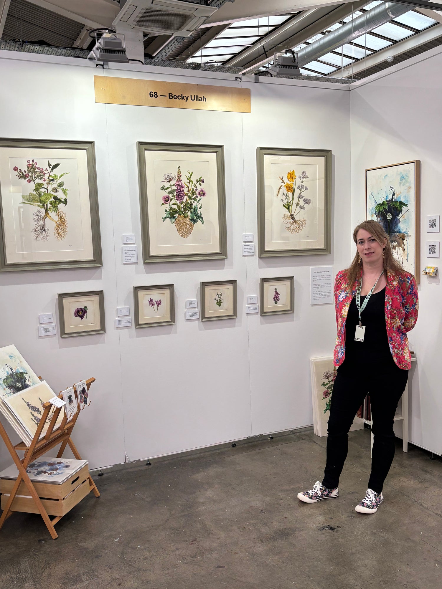Woman standing in an art exhibition with framed botanical artworks on the wall.